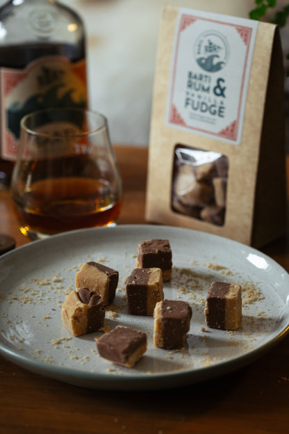 Fudge pieces on a plate with a glass of whiskey and a package labeled 'Bart's Rum & Raisin Fudge' in the background.